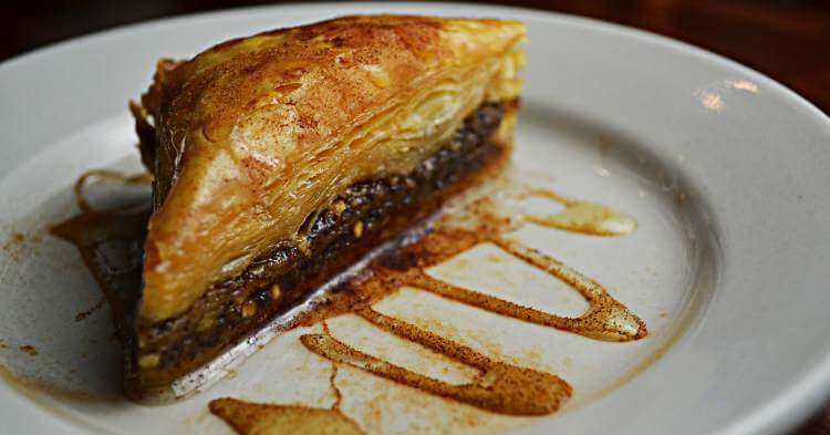 Parče baklave prelivene šećernim sirupom na belom tanjiru