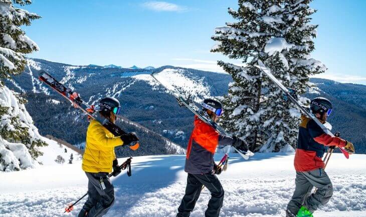 Tri skijaša na planini idu kroz sneg sa skijama u rukama
