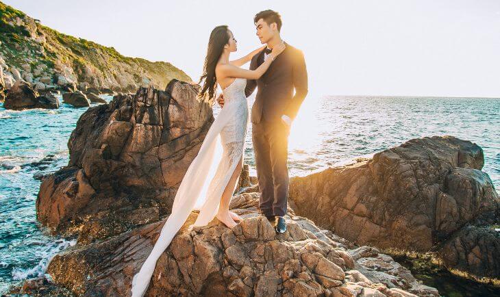 Mladenci stoje pored mora na stenama