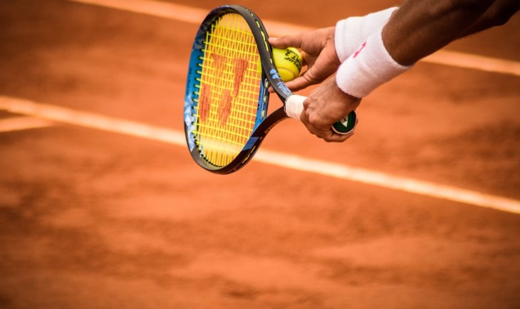 Čovek drži reket za tenis i lopticu.