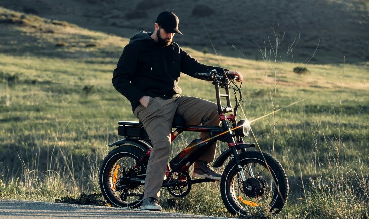 Covek na elktričnoj bicikli, iza njega poljana.