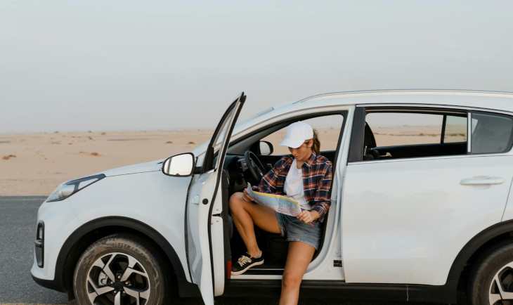 Žena sedi u automobilu i gleda u mapu.