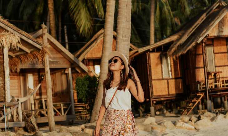 Žena sa šeširom šeta peščanom plažom.