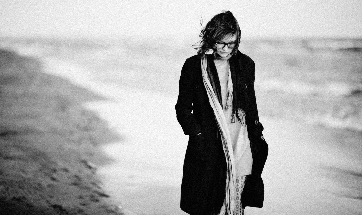 Devojka obučena u dug crni kaput šeta na plaži.