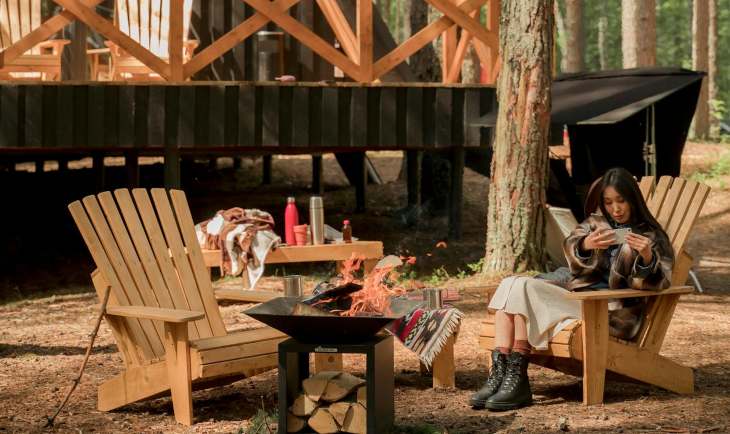 Devojka sedi ispred moderne brvnare u prirodi.