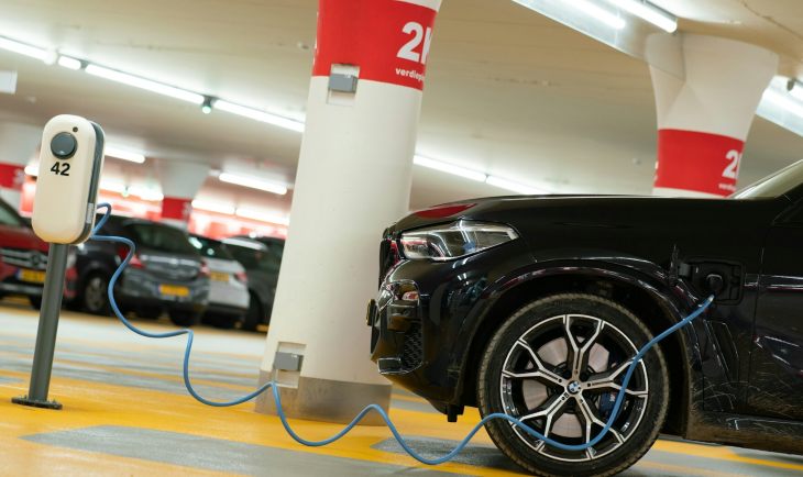 Crni auto priključen na električni punjač u garaži