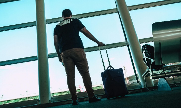 Čovek drži mali kofer i gleda kroz prozor na aerodromu