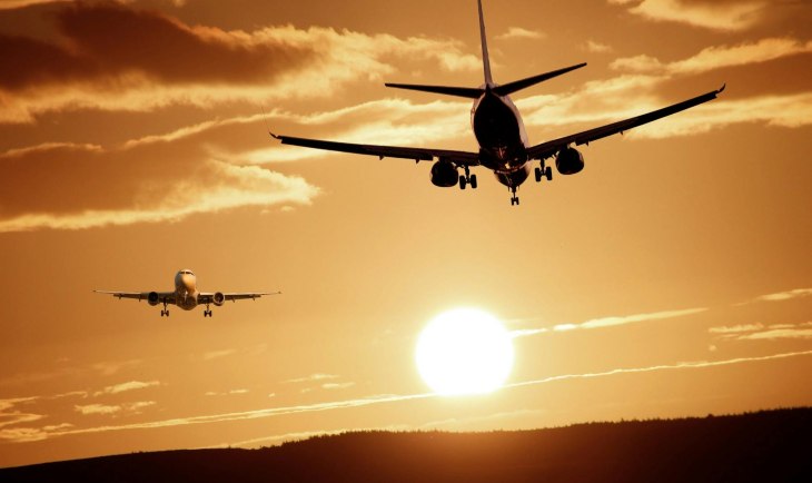 Dva aviona se mimoilaze na nebu iznad kopna uz zalazak sunca u pozadini