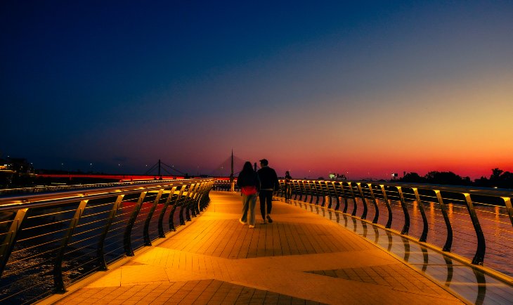 Dvoje ljudi šetaju na keju kod Beograda na vodi u večernjim satima