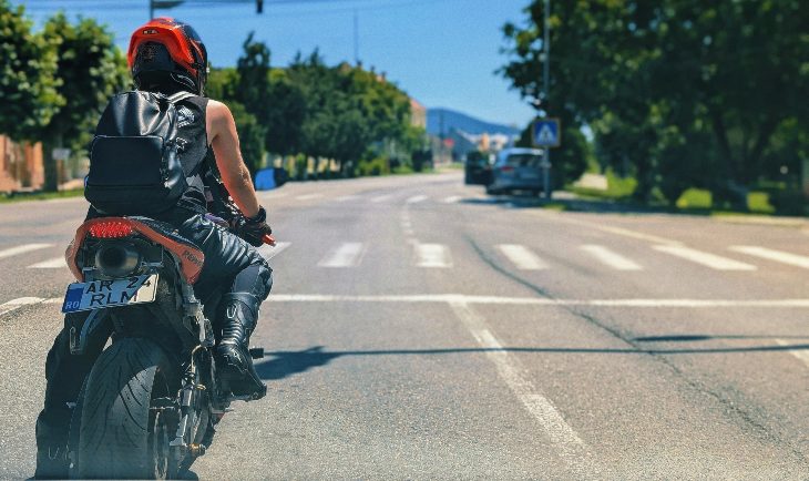 Čovek u kožnoj jakni i sa kacigom vozi motor na putu