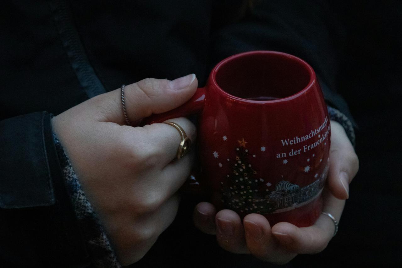 Ruke drže crvenu prazničnu šolju sa jelkom i belim zvezdicama.