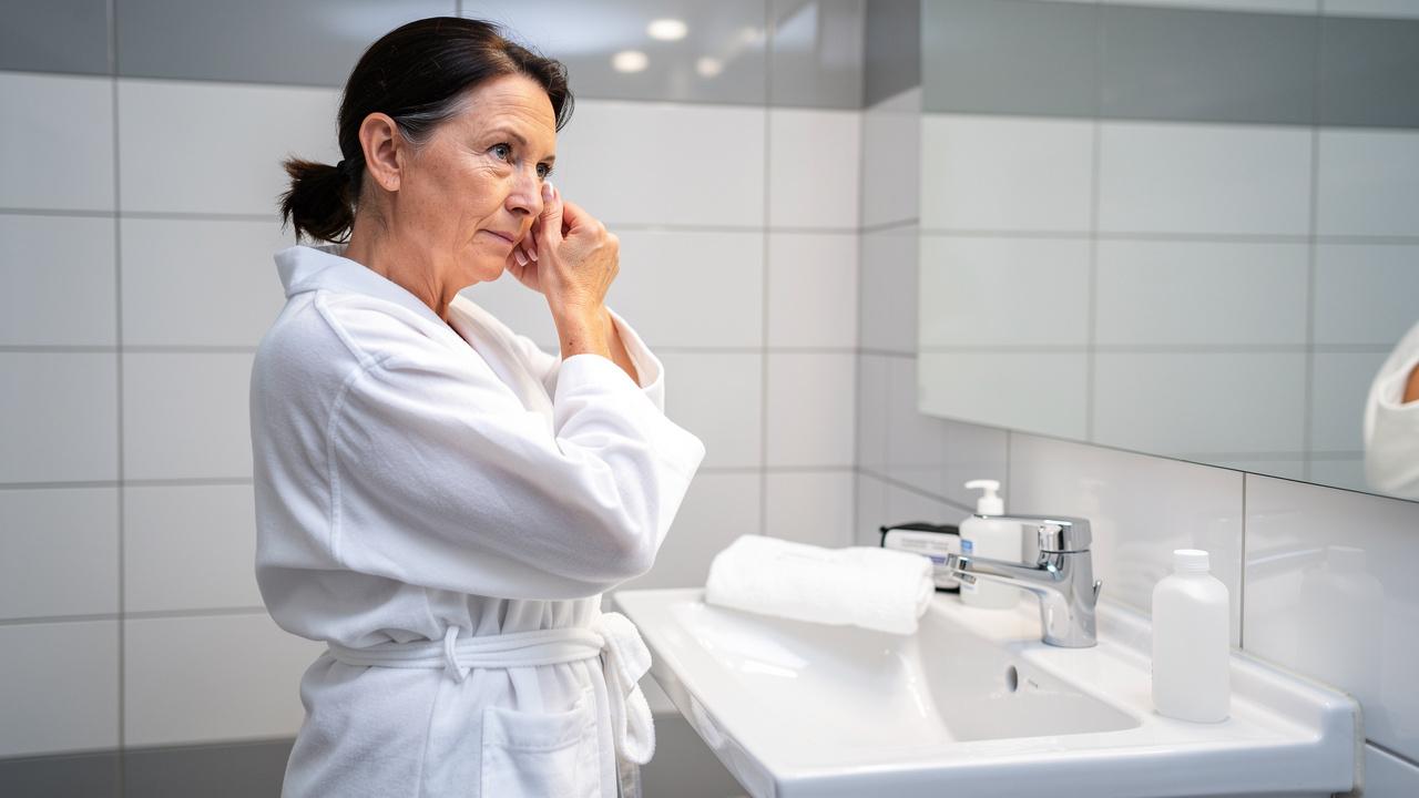 Žena u belom ogrtaču stoji pored lavaboa i dodiruje oko